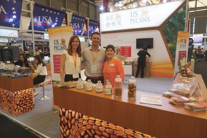 At the U.S. Pecans booth at SIAL China, the representatives smile and pose behind the counter, which is covered in brochures and pecans.