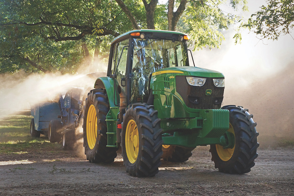 A green tractor pulls equipment through a pecan orchard during harvest season.