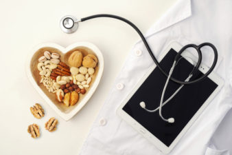 A heart-shaped bowl filled with a variety of tree nuts next to a doctor's coat and a stethoscope.