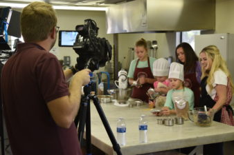 A group of women conducted a cooking demonstration while a camera crew captures the scene for the tv show "Chasing Down Madison Brown."