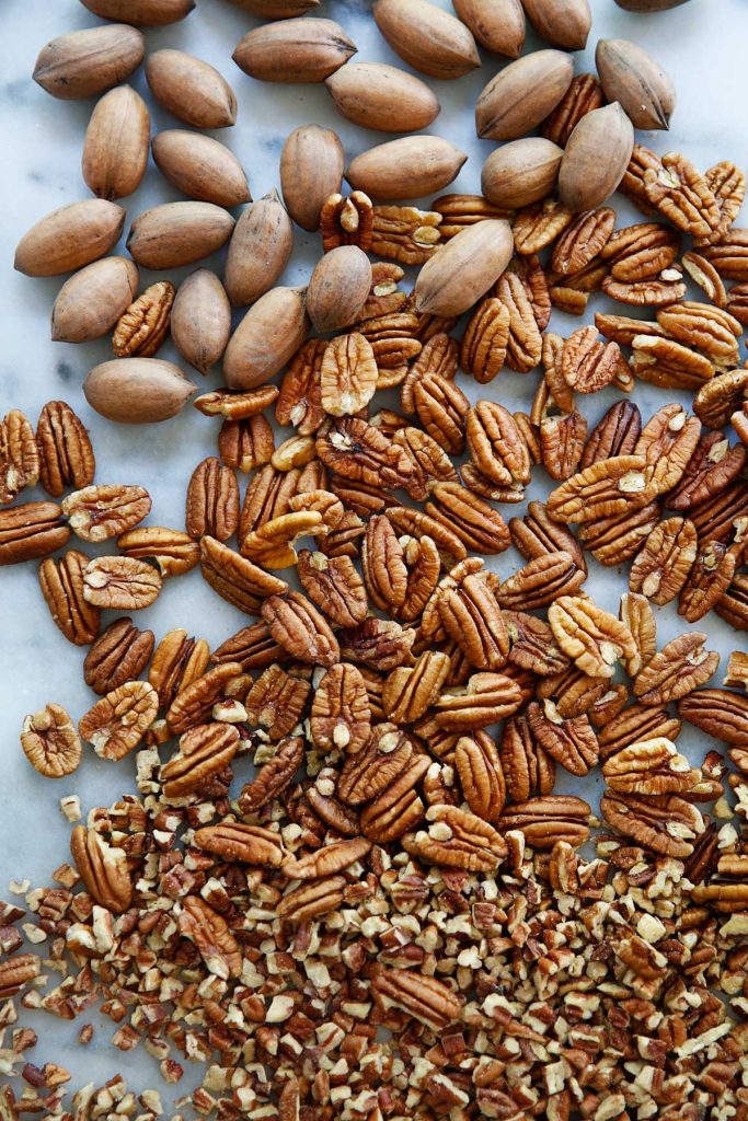 Pecan pieces transition to pecan halves and then inshell pecans on a marble countertop. At each level, industry members use practices that consumers want in food production.