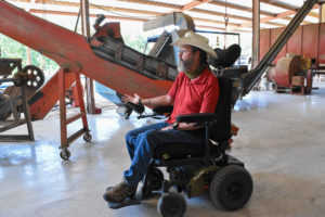 Charles Ewing in an electric wheelchair gestures at the nonprofit's gravity table in its pecan cleaning plant. Ewing cofounded 3SA for Veterans and this nonprofit orchard helps vets.