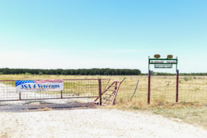 A cattle gate in front of a pecan orchard has a sign that reads 3SA for Veterans. To this sign's right, another sign sits that reads Eldorado Pecans. The nonprofit will use this pecan orchard to help vets.