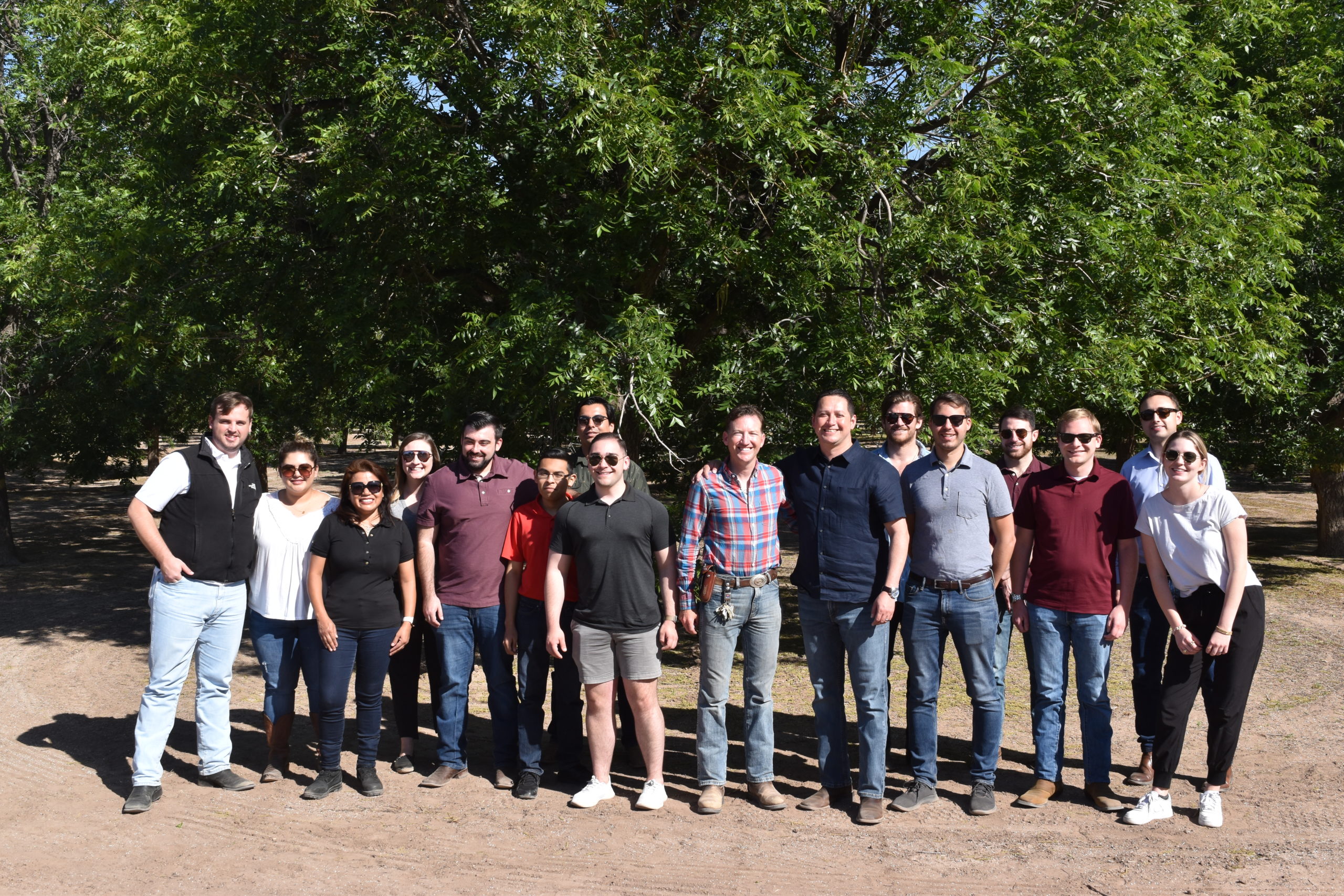 A group of people stand in front of mature pecan trees at an orchard in West Texas.