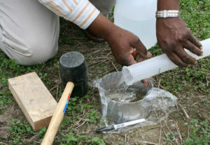 A man pours water into a metal ring while conducting an infiltration rate test in his farm in order to better understand the soil health.