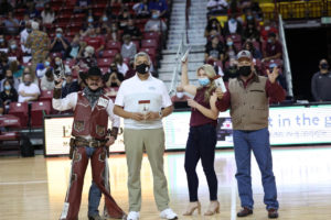 The mascot Pistol Pete poses with three people in NM State fan gear and introduces Pistol Pete's Pecans.
