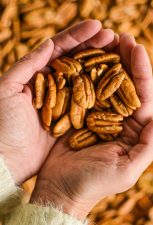 A woman holds a handful of golden brown pecan kernels.