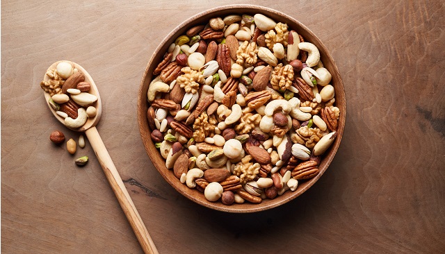 A wooden bowl filled with all sorts of tree nuts, including pecans, almonds, pistachios, macadamias, and cashews.