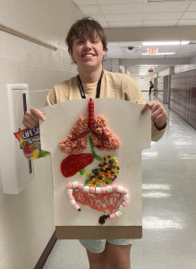 A high school boy holds up a poster that shows the human organ system made out of candy.
