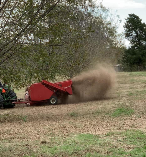 A pecan harvester kicks up dust while collecting nuts.